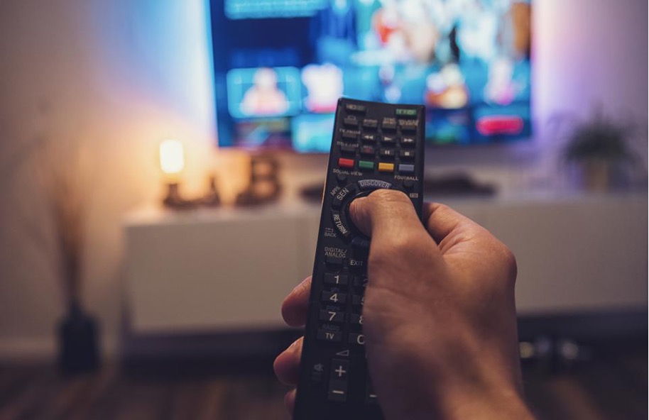 a hand holding a remote control which is aimed at at smart television